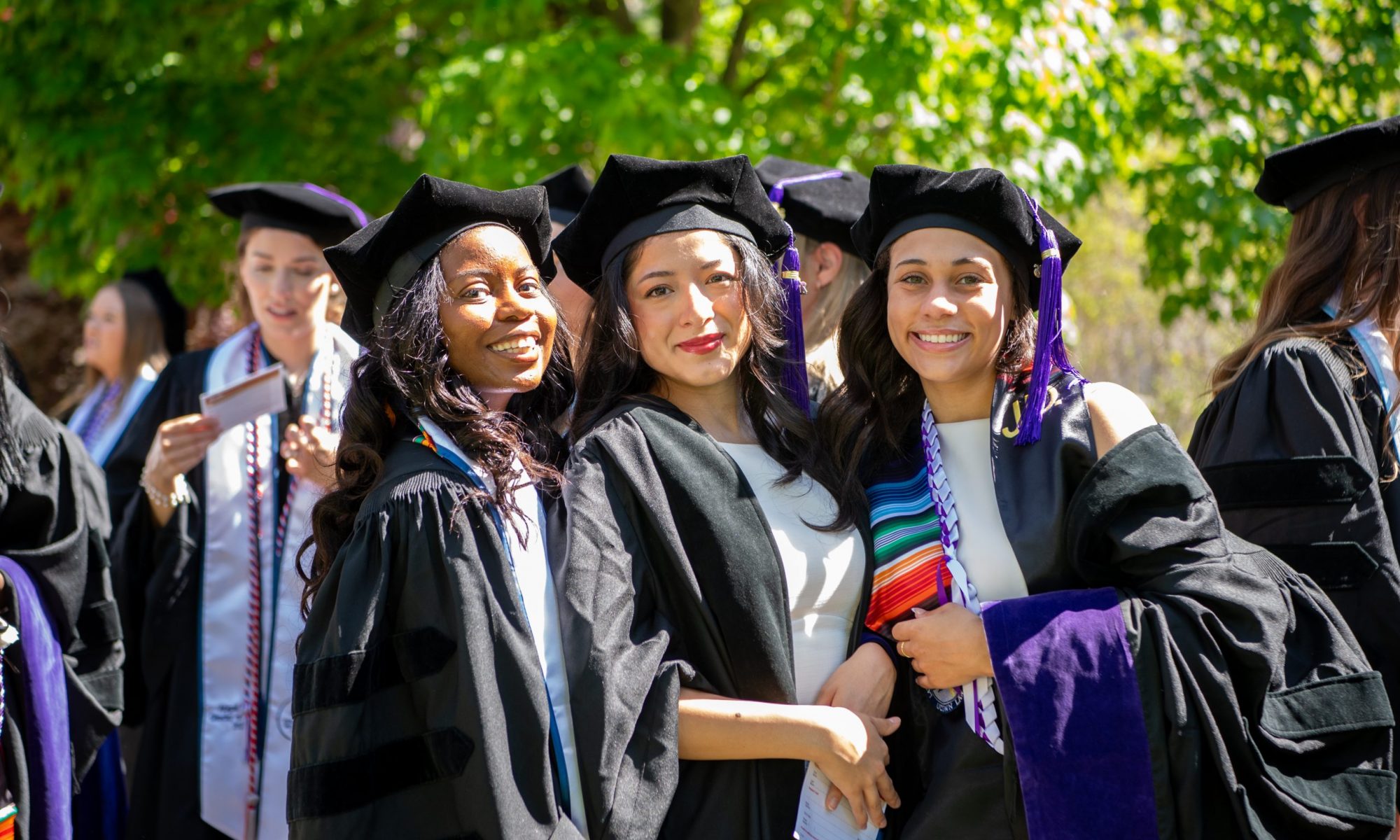 Three graduates in their regalia standing in a line.